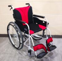 輪椅王 黑色和紅色的日本品牌 Miki MST43JL-22 手推輪椅配有大型後輪和腳踏板,位於灰色瓷磚地板上,靠著米色牆壁。