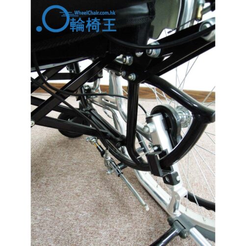 輪椅王 黑色 Miki LX-2 輪椅框架的特寫視圖，突出顯示其鎖定機構和舖有地毯的地板上的輪子組件。左上角可見「WheelChair.com.hk」標誌，展示了這款日本品牌Miki LX-2高背輪椅。