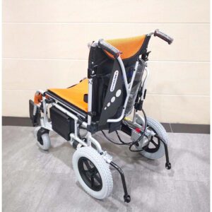 Le fauteuil roulant électrique Merits KP25.2 de la marque taïwanaise, roi des fauteuils roulants, est équipé d'un siège orange et d'un dossier noir et est situé devant le mur carrelé beige. Les fauteuils roulants électriques ont des roues arrière plus grandes, des roues avant plus petites et des commandes.