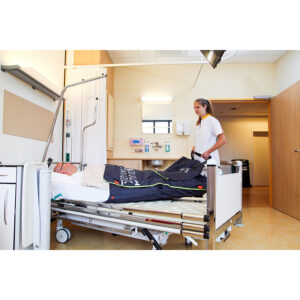 Wheelchair King A medical staff member stands beside a hospital bed, helping a patient covered with a blanket in a clean, modern ward.