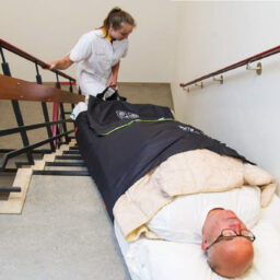 Les ambulanciers paramédicaux de Wheelchair King utilisent des dispositifs spéciaux d'évacuation des escaliers pour aider les personnes âgées enveloppées dans des boucliers de protection à descendre les escaliers.