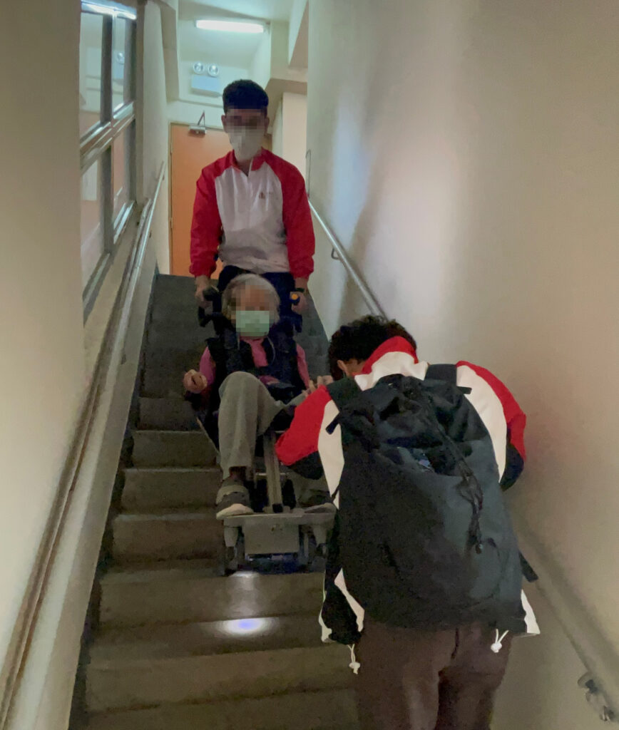 The Wheelchair King duo uses the Wheelchair King stair lift to assist seated people down the stairs.