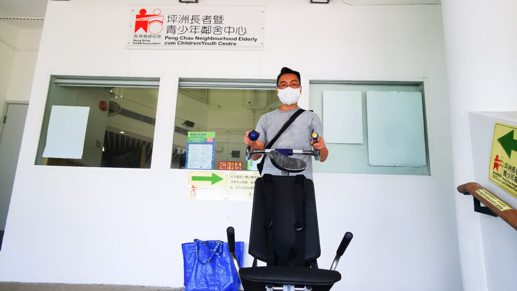 車椅子王 平洲老人・児童・青少年センターの車椅子王階段リフトの外で、マスクをした男性がリカンベント自転車で運動している。