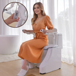 【車いすの王様】SLDのトイレ昇降椅子にオレンジ色のドレスを着た女性が座っています。拡大図は、ボタンのあるコントロール パネルを持っている手を示しています。明るいバスルームになりそうな雰囲気です。