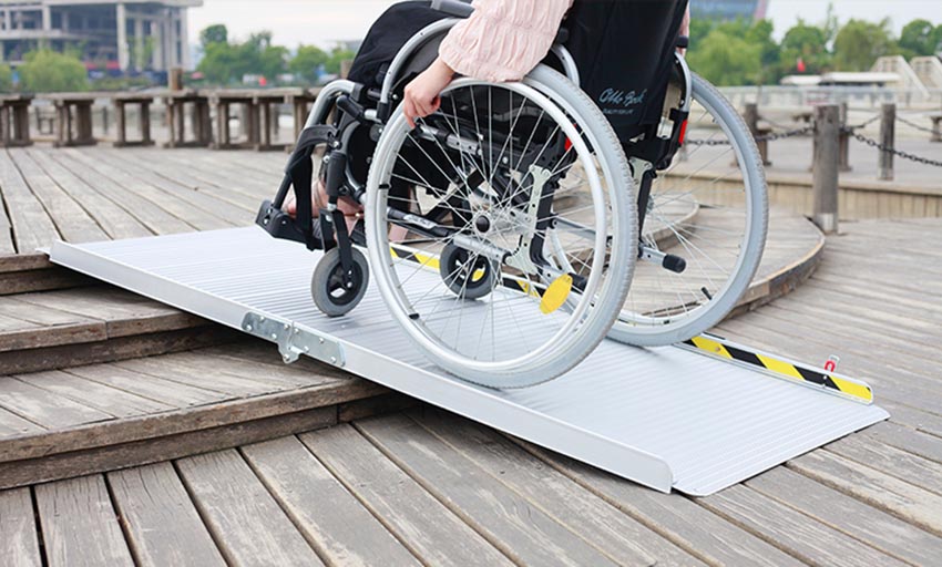 [Wheelchair King] A wheelchair user climbs up a portable ramp on a wooden deck, demonstrating the versatility of folding high-strength aluminum alloy ramps.