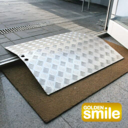 [Wheelchair King] The aluminum ramp on the threshold is on a brown mat, with a stylish "Golden Smile Gym Board M209 (56)" logo on the bottom corner, adding a touch of elegance.